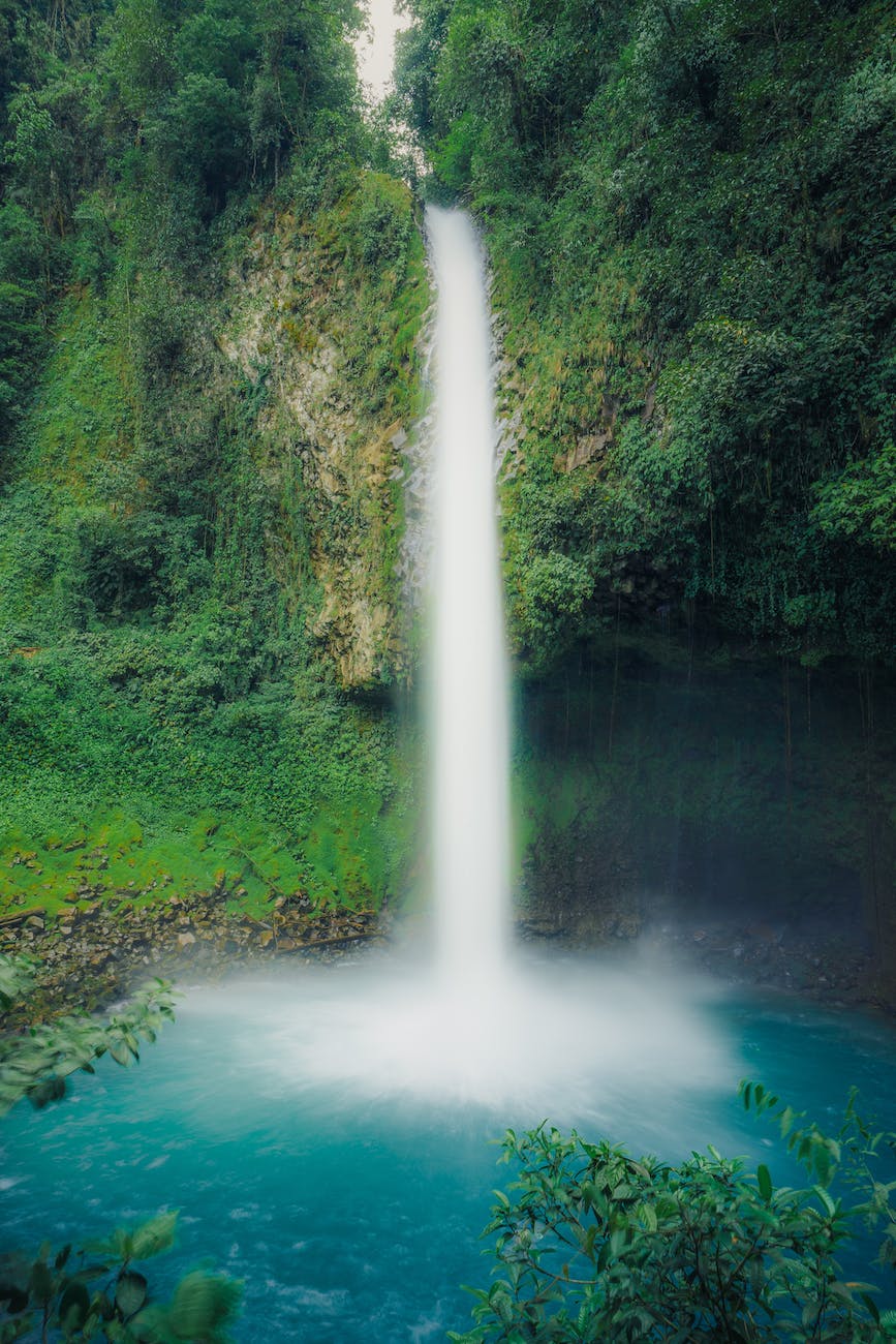 waterfall cascades into blue lagoon, surrounded by greenery, moss, and cliffs