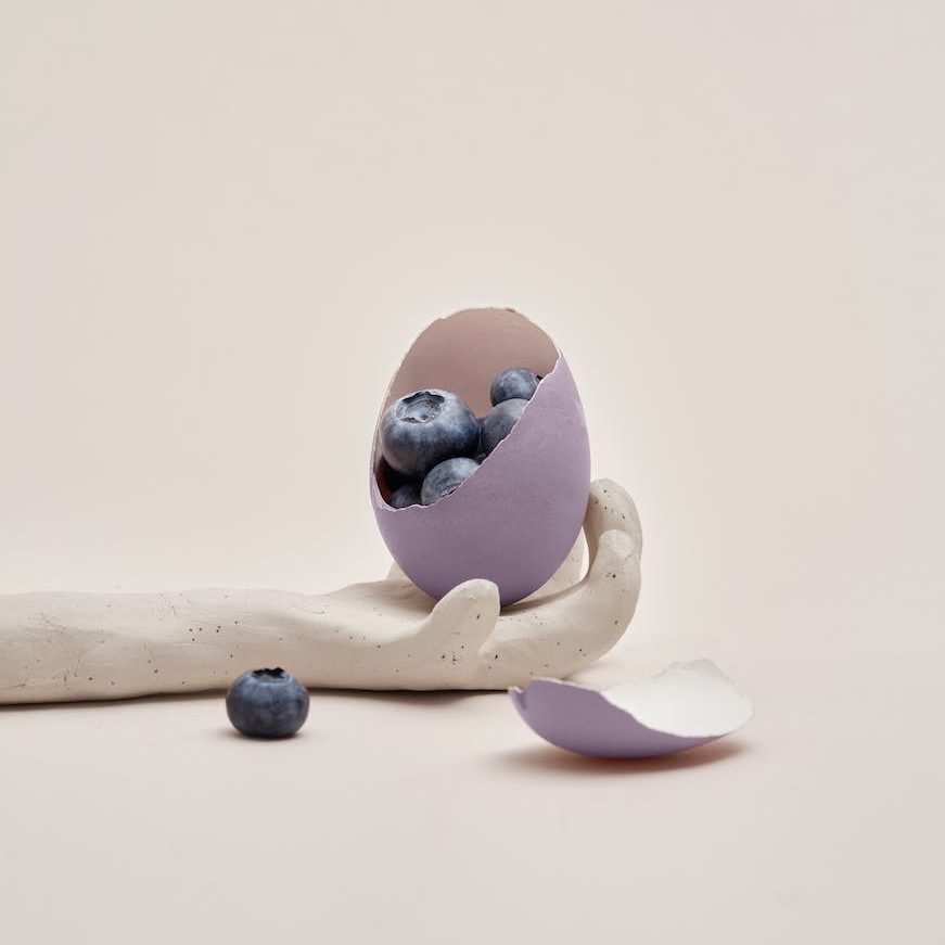 blueberries sit in purple eggshell inside the hand of a marble statue