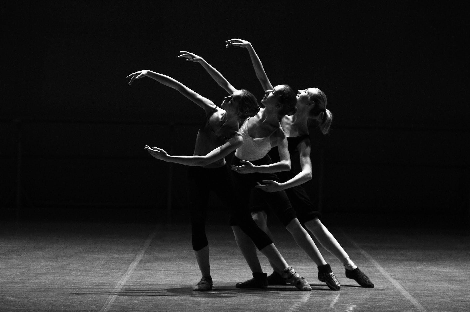 three dancers gracefully pose with arms outstretched, mimicking each other